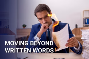 Man at a desk with piles of papers. Holding one paper on fire. Text in foreground reads: 'Moving Beyond Written Words'